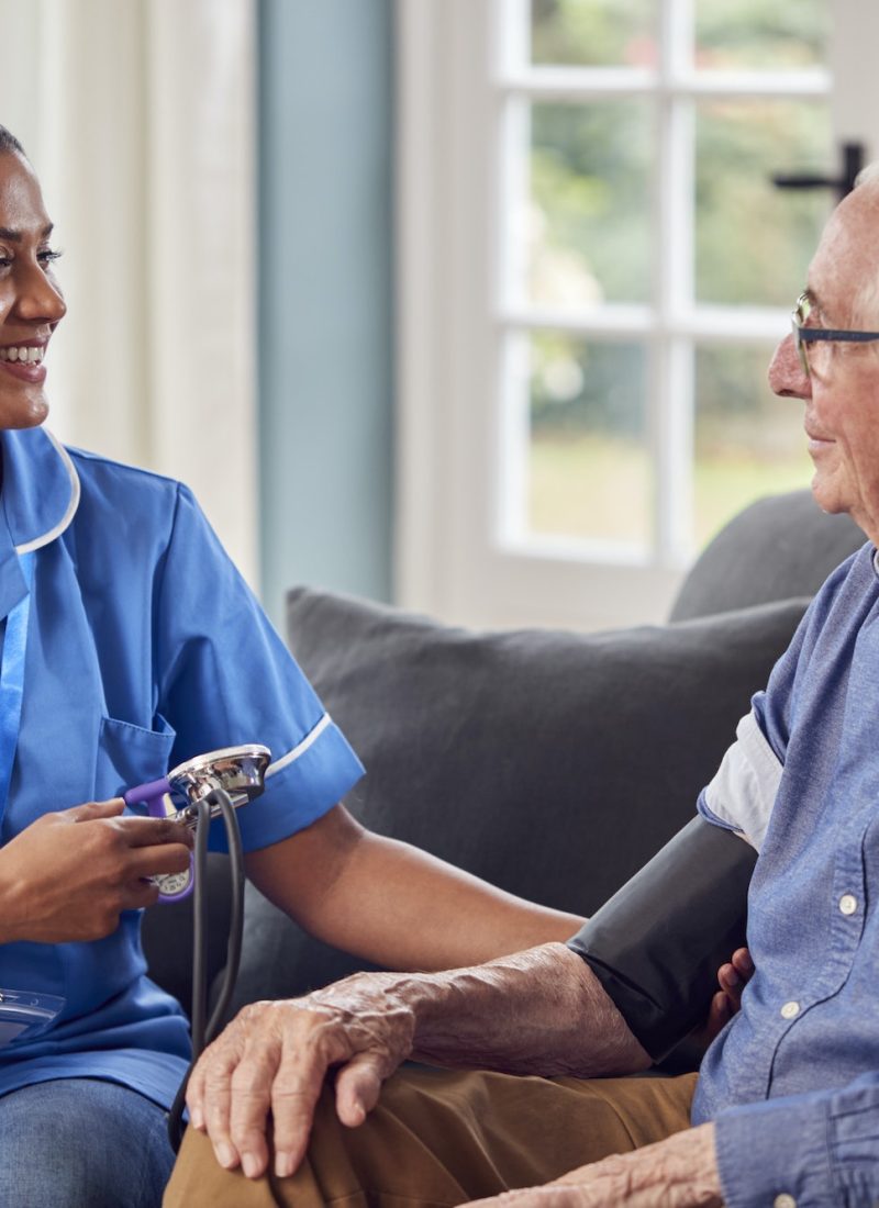 senior-man-at-home-in-lounge-having-blood-pressure-taken-by-female-care-worker-in-uniform.jpg